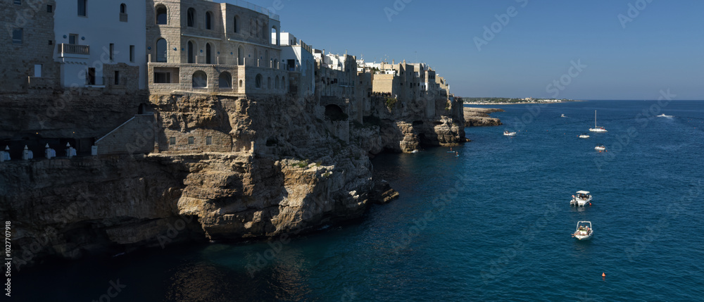 Fototapeta premium Fishing boat in the sea. Coastline. Rocky shore with buildings in Polignano a Mare, Italy.
