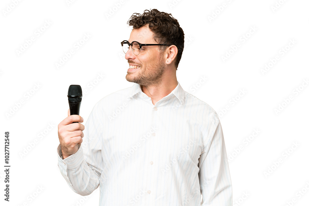 Brazilian man picking up a microphone over isolated chroma key background looking side Brazilian man picking up a microphone over isolated chroma key background looking side