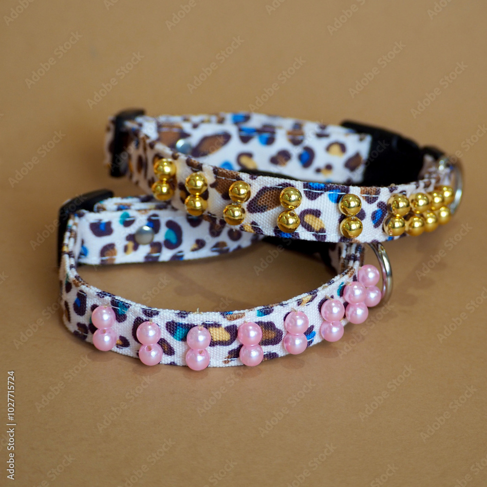 On a brown background lie two collars in leopard color with sewn-on beads of gold and pink color accessories for pets. collar for dogs On a brown background lie two collars in leopard color with sewn-on beads of gold and pink color accessories for pets. collar for dogs