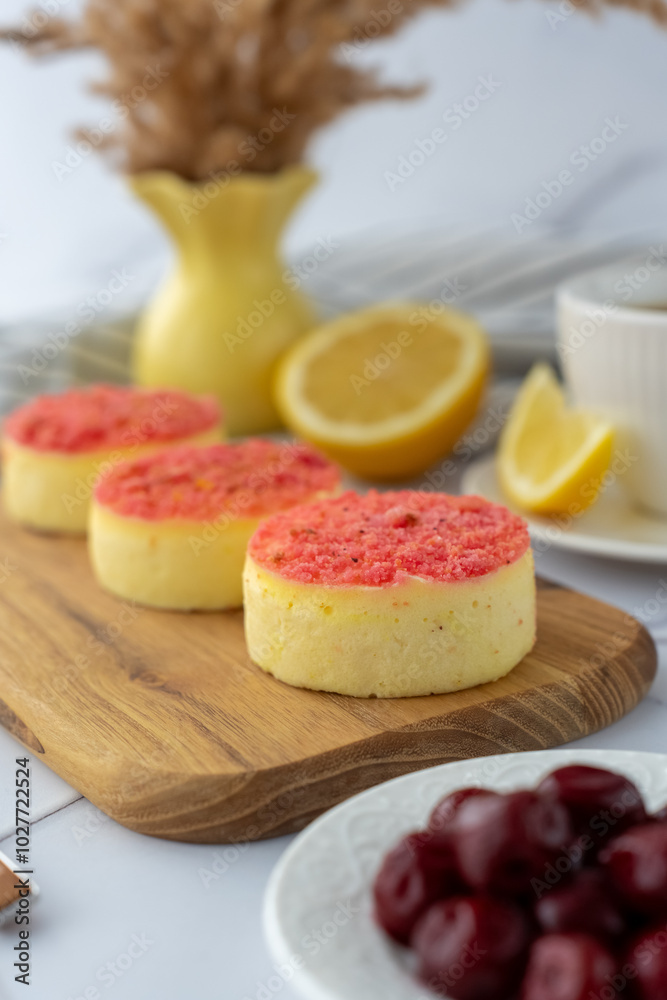 Mini cheesecakes with pink crumble topping served on a wooden board with lemons and cherries. Concept of summer dessert, fresh flavors, and artisanal pastries. Mini cheesecakes with pink crumble topping served on a wooden board with lemons and cherries. Concept of summer dessert, fresh flavors, and artisanal pastries.