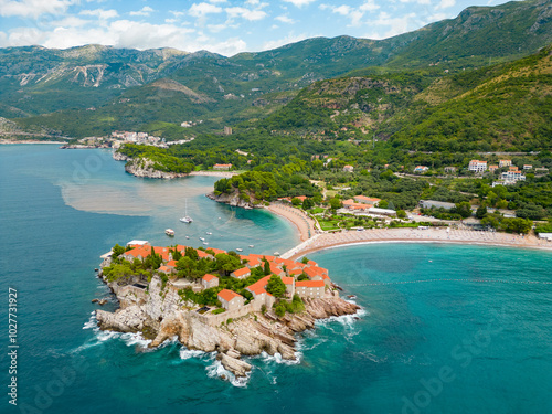 Aerial drone view of Sveti Stefan Island- Luxury travel destination in Montenegro. Waves splashing the rocks. At right is Sveti Stefan Beach. Panoramic view. Emerald water. photo