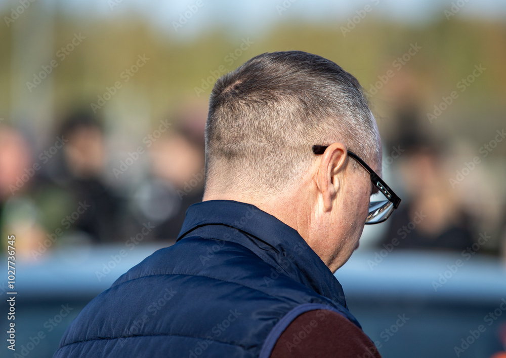 A man with a shaved head and glasses is standing in front of a car A man with a shaved head and glasses is standing in front of a car