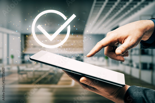 Close up of male hand pointing at tablet with digital Guarantee Checkmark on blurry office background. Compliance with regulations services and standards. photo