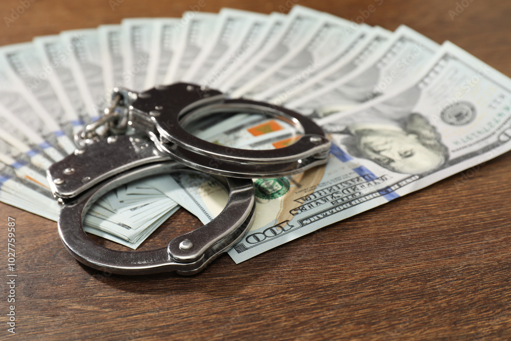 Handcuffs with dollar banknotes on wooden table, closeup Handcuffs with dollar banknotes on wooden table, closeup