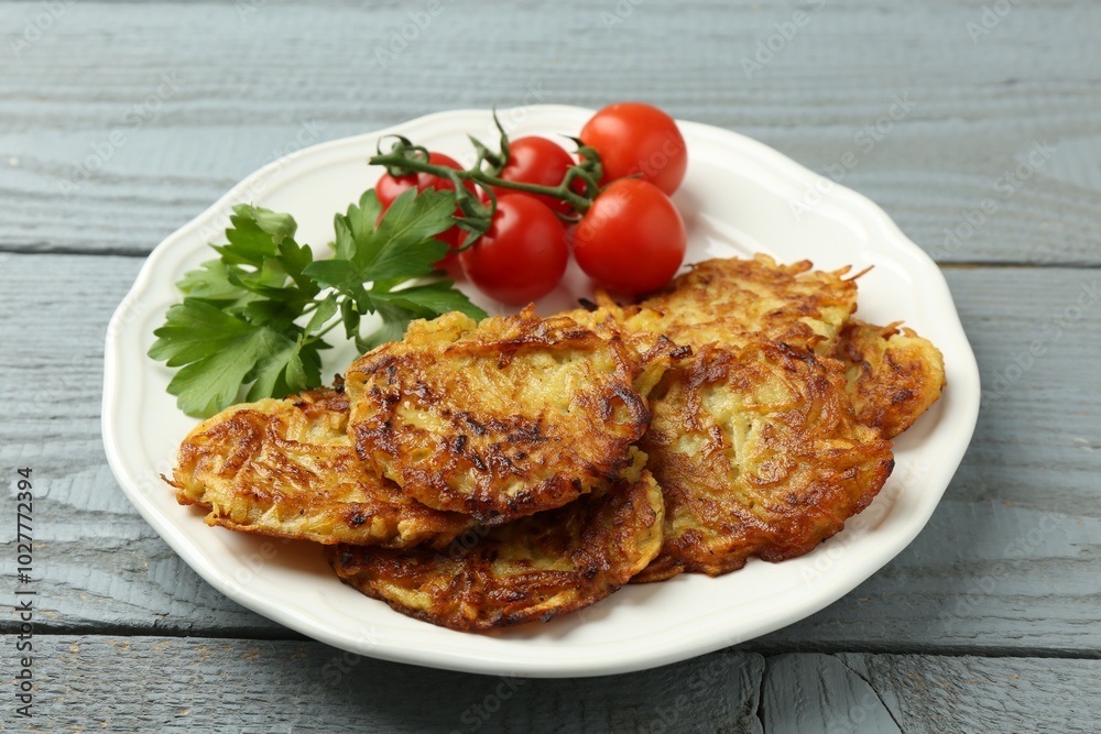 Delicious potato pancakes, tomatoes and parsley on gray wooden table, closeup Delicious potato pancakes, tomatoes and parsley on gray wooden table, closeup