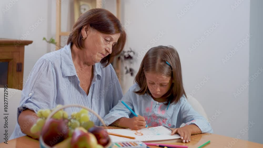 Grandmother guides her granddaughter as they engage in drawing together. The room is filled with natural light and a warm atmosphere, fostering creativity and bonding. Grandmother guides her granddaughter as they engage in drawing together. The room is filled with natural light and a warm atmosphere, fostering creativity and bonding.