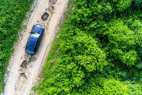 a car carefully navigating around a series of potholes on a damaged rural road, viewed from above.