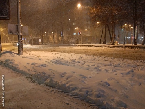 A quiet city street blanketed in snow during the night. Soft streetlights cast a warm glow over the snowy scene, creating a tranquil and peaceful winter atmosphere.