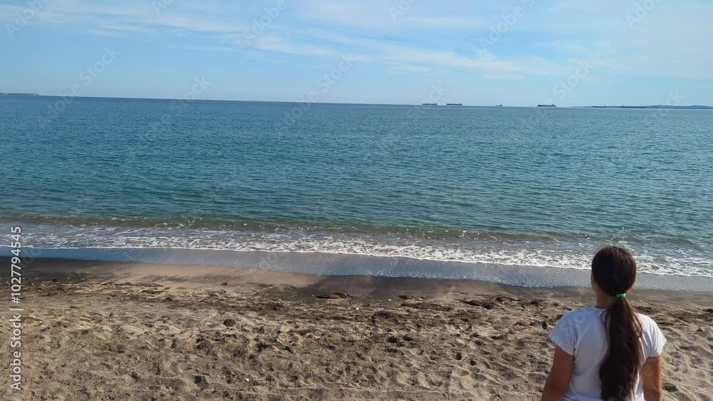 A woman in shorts and a hat walking along the sandy beach on a clear sunny day. A woman in shorts and a hat walking along the sandy beach on a clear sunny day.