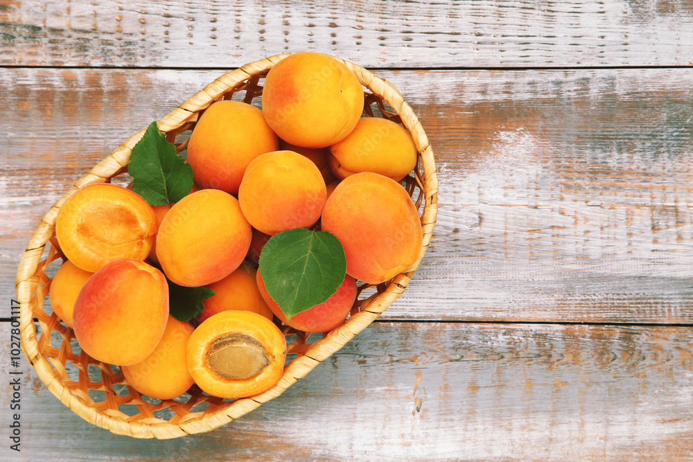 Sweet apricots with leaves in basket on wooden background