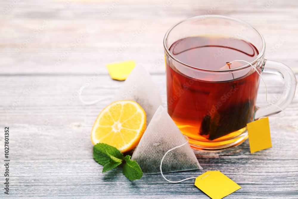 Cup of tea with tea bags, mint leafs and lemon on wooden table