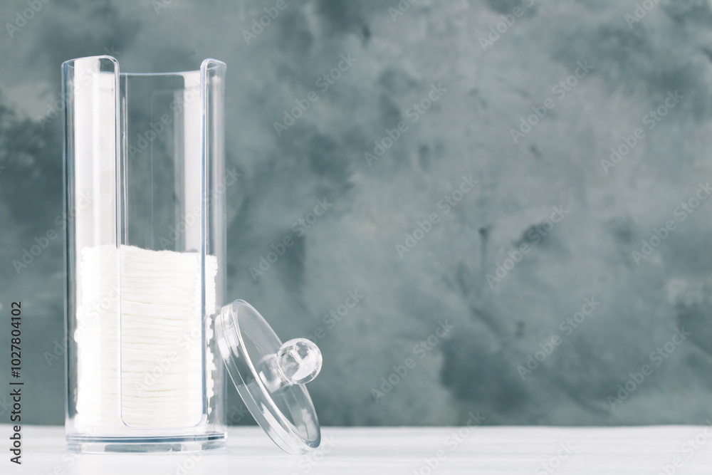 Cotton pads in plastic jar on grey background