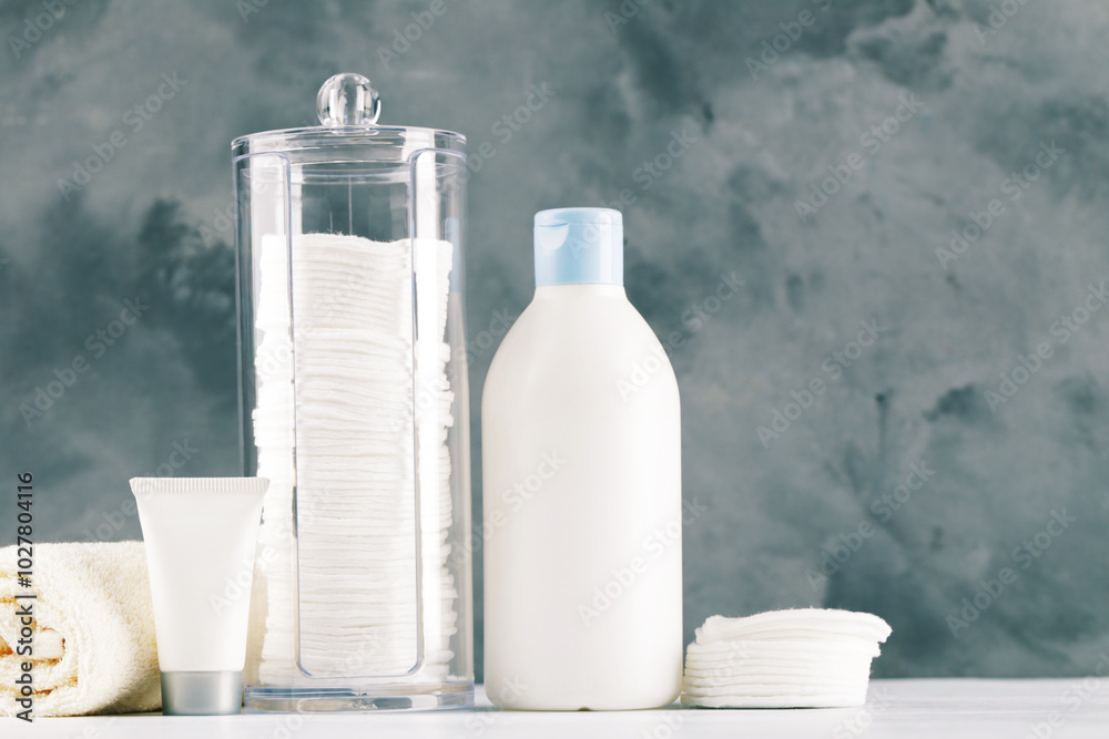 Cotton pads in plastic jar and bottles with towel on grey background