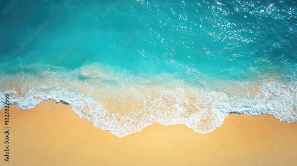 Top view of a sunny coastline with bright blue sea water and gentle waves lapping onto soft, golden sand