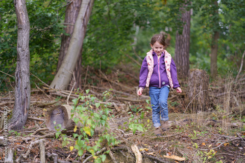 Little beautiful girl in a hoodie and vest against the background of a dark autumn forest. Concept of a happy childhood in nature