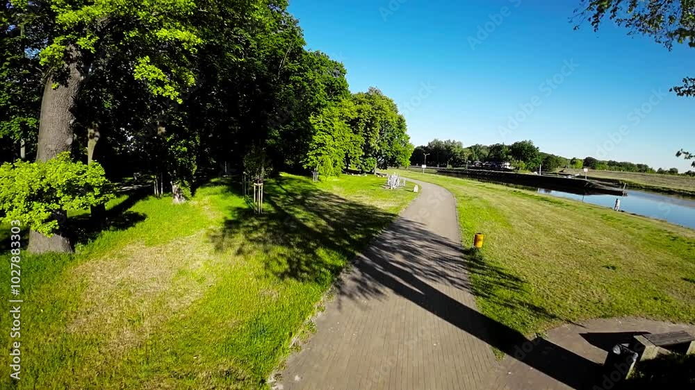 A beautiful park in Opole, Poland, with lush green trees, a paved path, and a tranquil river running alongside it. The park is a popular spot for locals and tourists alike, offering a peaceful and A beautiful park in Opole, Poland, with lush green trees, a paved path, and a tranquil river running alongside it. The park is a popular spot for locals and tourists alike, offering a peaceful and