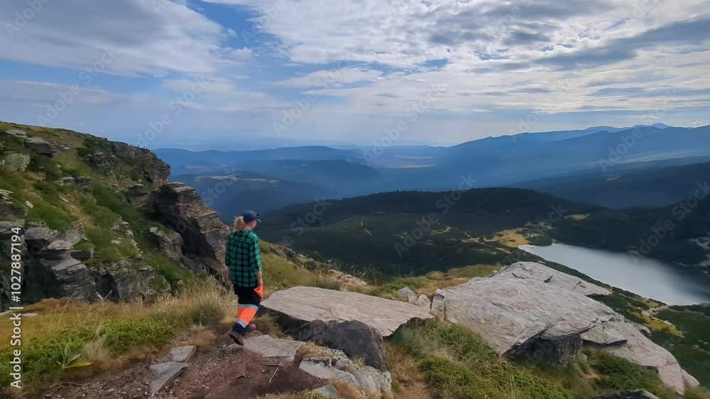 A person walks through the mountains, surrounded by rocks and alpine lakes, in hiking gear with trekking poles, enjoying the views and active outdoor adventure in the Rila region of Bulgaria. A person walks through the mountains, surrounded by rocks and alpine lakes, in hiking gear with trekking poles, enjoying the views and active outdoor adventure in the Rila region of Bulgaria.