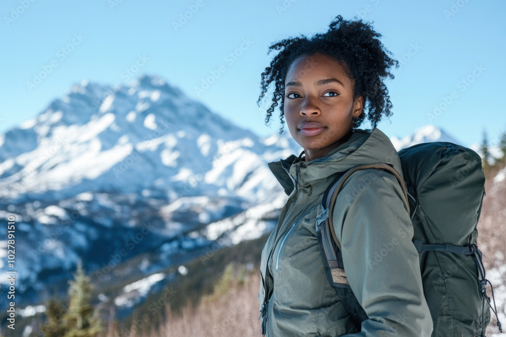 Black woman in grey jacket hiking in a snowy mountain range with clear blue skies Black woman in grey jacket hiking in a snowy mountain range with clear blue skies