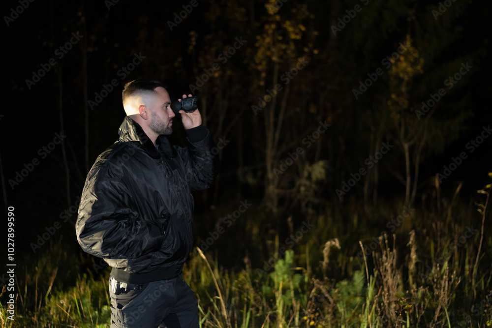 Obraz premium A man with a night vision device in his hand in a dark forest at night.