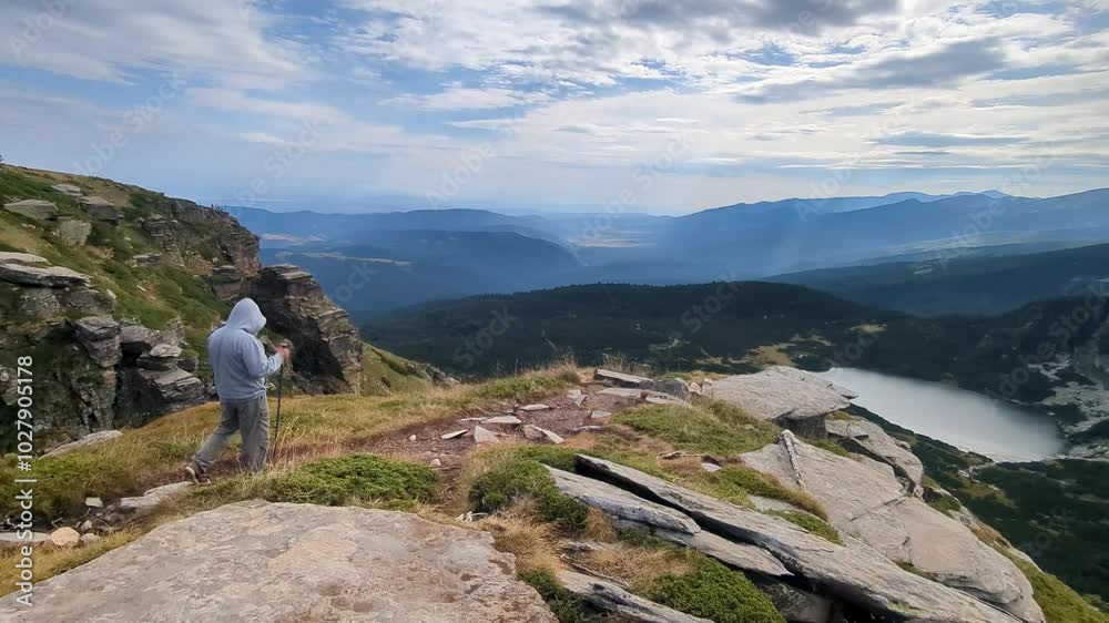 A person in athletic gear with a trekking poles walking along a trail in mountainous terrain, surrounded by beautiful scenery A person in athletic gear with a trekking poles walking along a trail in mountainous terrain, surrounded by beautiful scenery