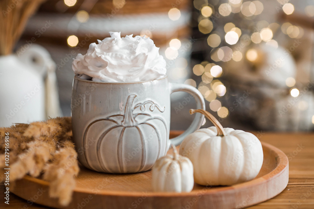 Delicious pumpkin latte with whipped cream and cinnamon in a mug on the table in the living room interior. Autumn decor in the house. Scandinavian style.