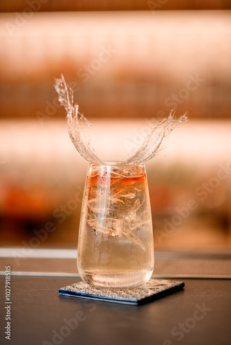 Focus on a glass of clear drink with ice, on a square stand, decorated with a decorative decoration in the shape of hay photo