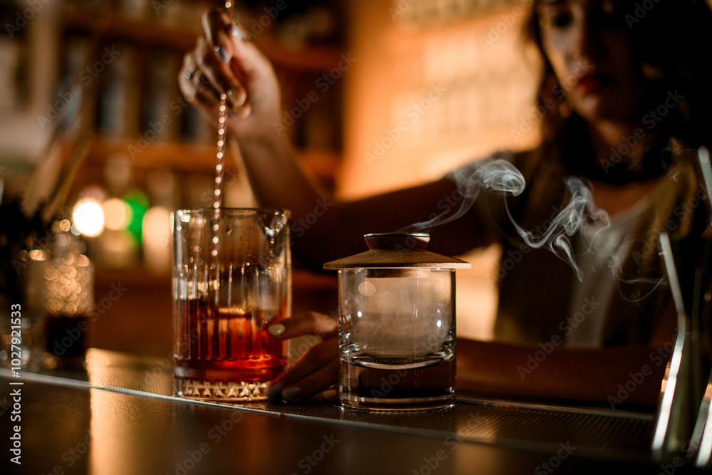 Focus on two glasses on the bar counter, in one of which a female bartender is stirring a cocktail Focus on two glasses on the bar counter, in one of which a female bartender is stirring a cocktail