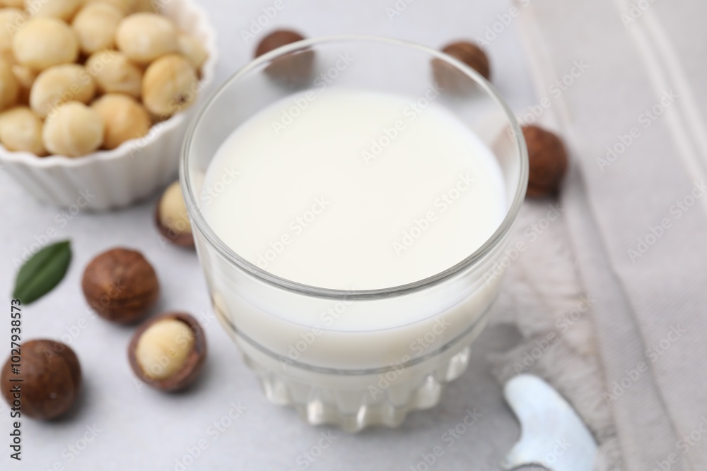 Glass of macadamia milk and nuts on white table, closeup Glass of macadamia milk and nuts on white table, closeup