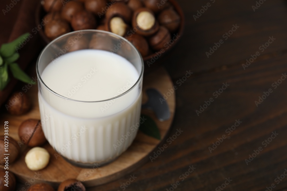 Glass of macadamia milk and nuts on wooden table, space for text