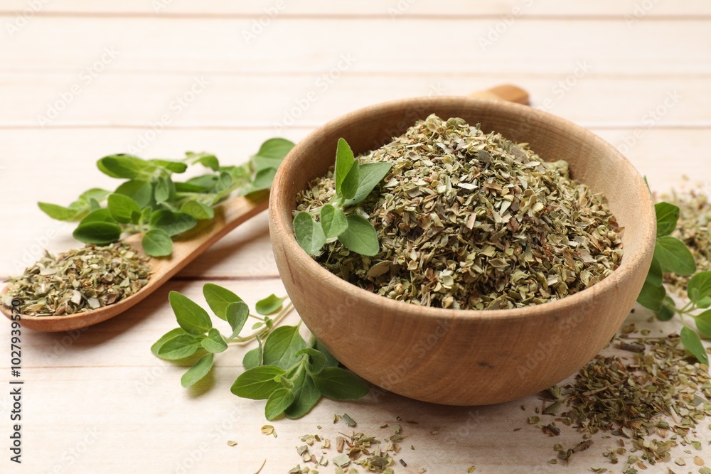 Dried oregano in bowl, spoon and green leaves on wooden table, closeup Dried oregano in bowl, spoon and green leaves on wooden table, closeup