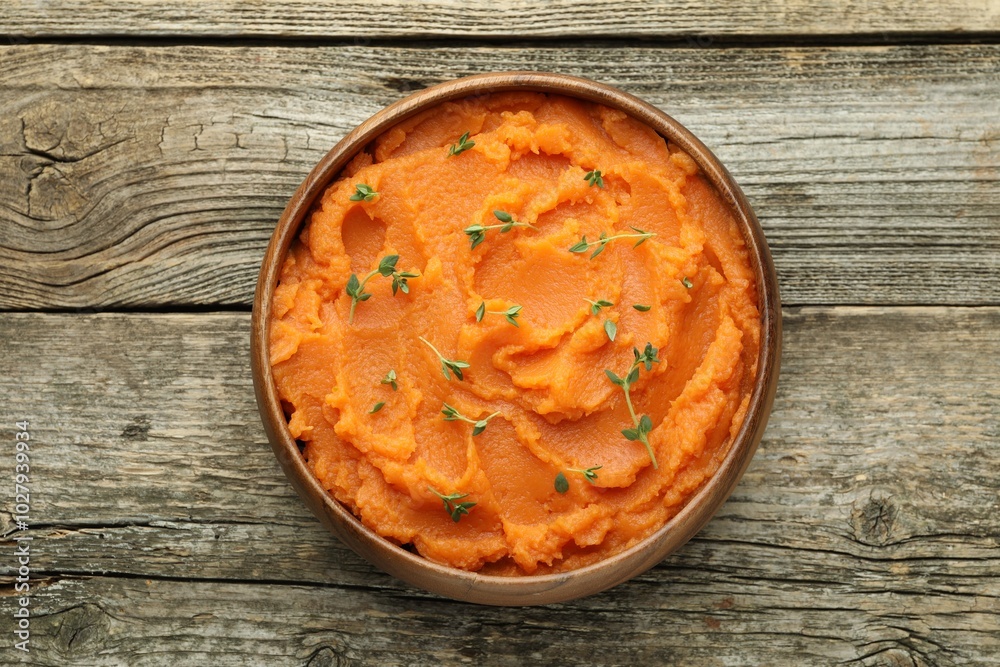 Tasty mashed sweet potato with thyme in bowl on wooden table, top view