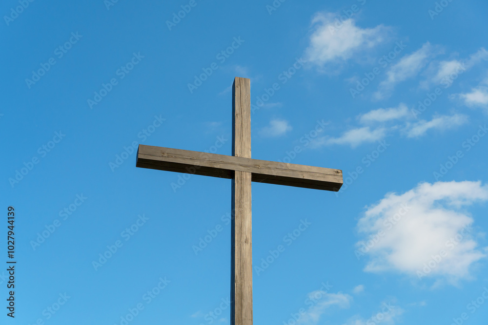 An Orthodox wooden cross on a background of blue sky and clouds. An old antique cross close-up. An Orthodox wooden cross on a background of blue sky and clouds. An old antique cross close-up.