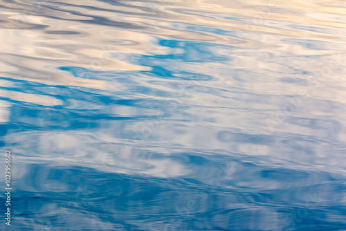Close up macro photo of waves on water surface blurred ripples. Transparent defocus blue and white colored water with ripples spreading in a shiny pattern on the surface background.
