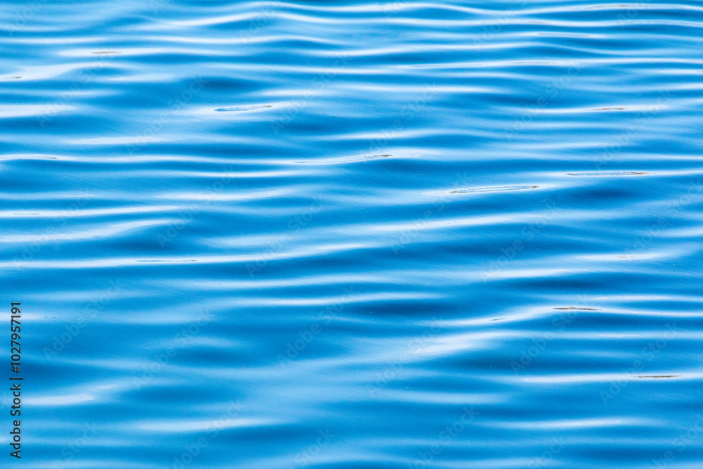 Close up of ripple wave patterns on blue water surface. Light and dark texture pattern, blurred defocus shining water surface background.
Close up of ripple wave patterns on blue water surface. Light and dark texture pattern, blurred defocus shining water surface background.