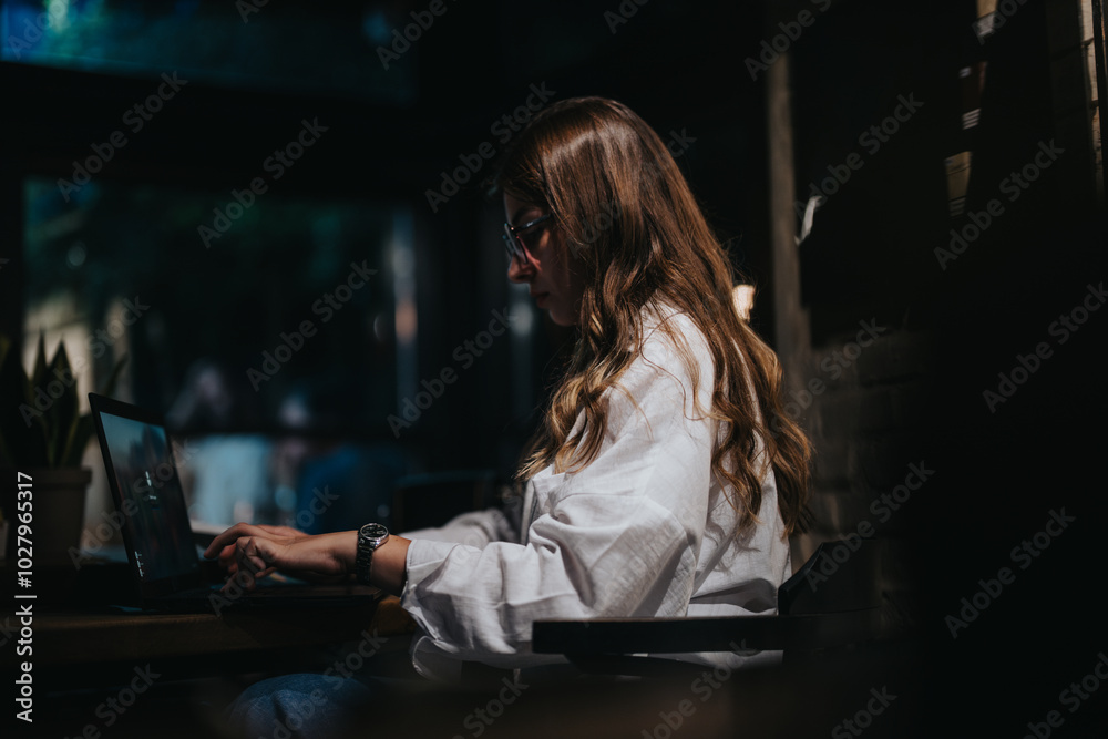 A dedicated businesswoman working on her laptop in a dark room, emphasizing concentration and productivity. A dedicated businesswoman working on her laptop in a dark room, emphasizing concentration and productivity.