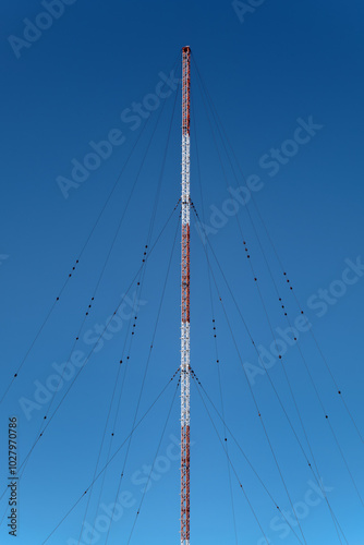 A tall radio antenna or communication tower with red and white stripes, supported by guy wires. It extends vertically and is likely used for transmitting radio signals, TV, or telecommunications.
