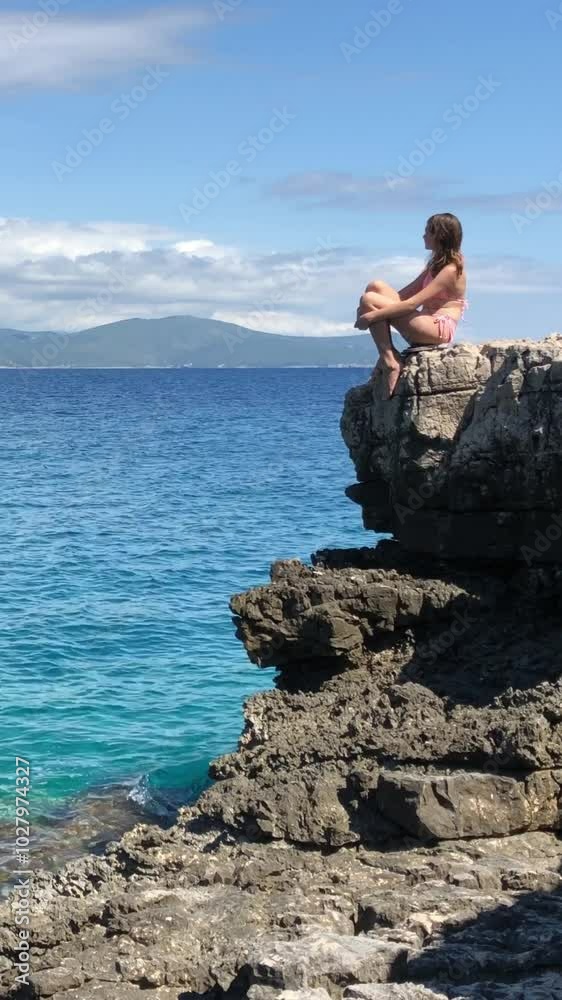Girl with a perfect figure seats on the empty rocky shore Girl with a perfect figure seats on the empty rocky shore