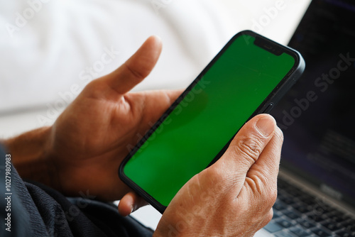 A close-up of a hand holding a smartphone with a green screen, ideal for mockups or design insertions photo