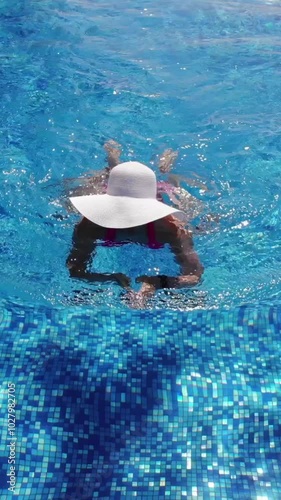 Young woman in white hat swimming in blue pool