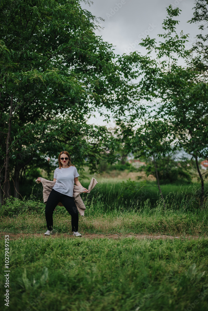 A woman stands confidently in a lush green forest park, enjoying the serene and natural surroundings. She appears relaxed and content in the peaceful outdoor setting. A woman stands confidently in a lush green forest park, enjoying the serene and natural surroundings. She appears relaxed and content in the peaceful outdoor setting.