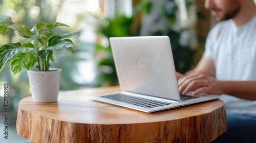 In a serene indoor setting, a person engages with a laptop placed on a circular wooden table, highlighting the blend of nature and modernity with ambient greenery.