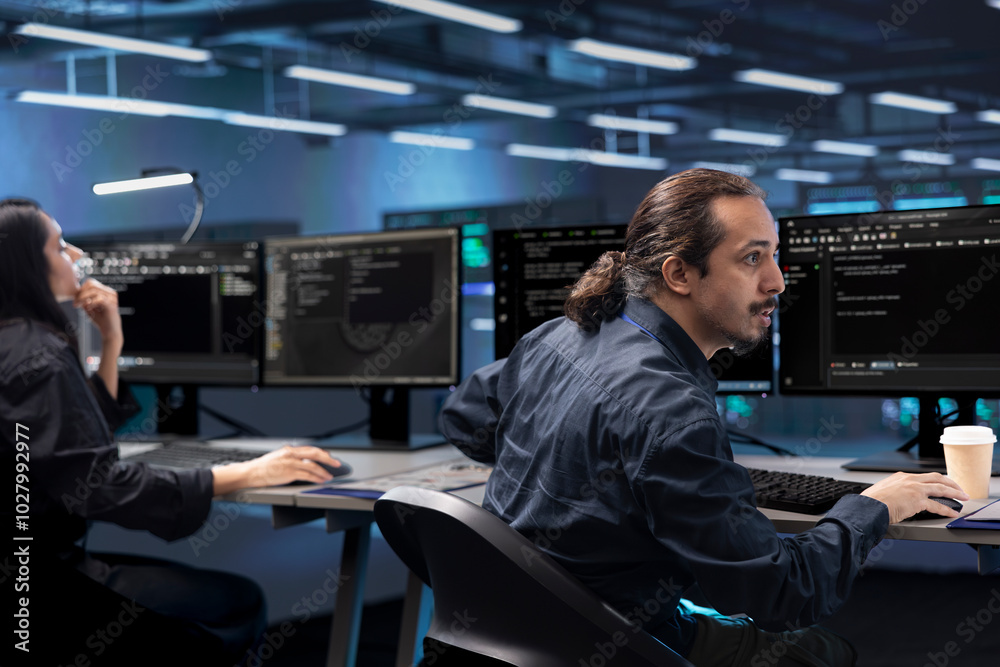 Colleagues in data center facility running system diagnostic tests on computers. IT experts at PC desk in server farm deploying error checking utilities to mend network issues Colleagues in data center facility running system diagnostic tests on computers. IT experts at PC desk in server farm deploying error checking utilities to mend network issues