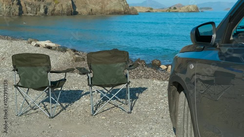 Autocamping by the sea. Two empty chairs sit on a rocky beach beside a parked car, facing the ocean. Mountains rise in the distance, creating a peaceful and serene atmosphere perfect for relaxation photo