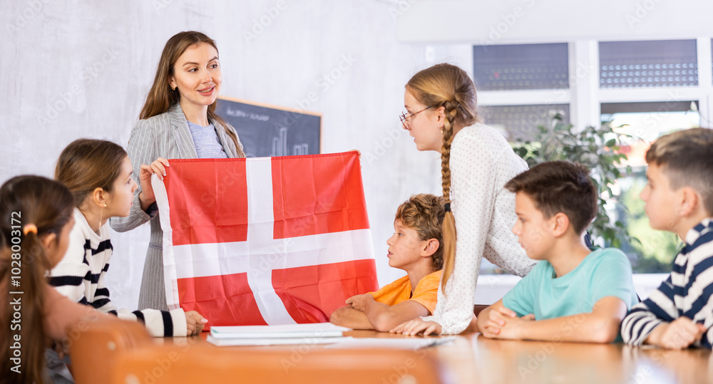 Obraz premium Decent teacher showing Denmark flag to group of preteen schoolchildren in classroom during lesson