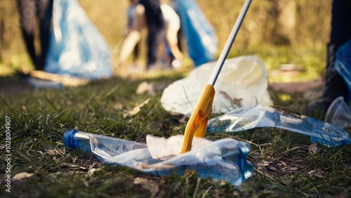 Photos Group of volunteers cleaning the forest from litter and plastic waste, grabbing trash and junk with a long claw tool