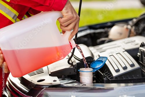 Close-up service worker man driver pouring red non freezing windshield cleaning glass washer fluid in hood car tank from canister bottle. Summer or winter fluid windscreen liquid glass window cleaner photo