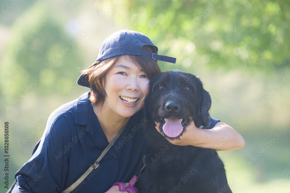 緑がきれいな場所でペットの大型犬と飼い主の女性　カメラ目線のクローズアップ