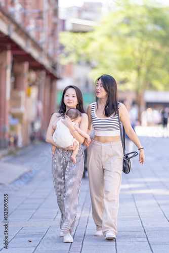 Two Taiwanese women in their 30s wearing casual outfits walk along Dihua Street in Taipei City, Taiwan, in September, each holding a 6-month-old baby.