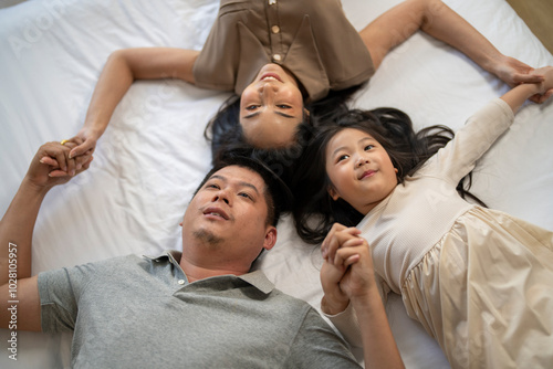 A joyful mother and daughter laughing together while lying on a bed. The playful moment showcases their strong bond and happiness in a comfortable home setting, surrounded by natural decor.