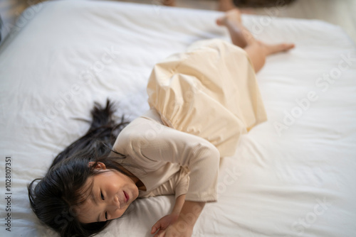 A joyful mother and daughter laughing together while lying on a bed. The playful moment showcases their strong bond and happiness in a comfortable home setting, surrounded by natural decor.